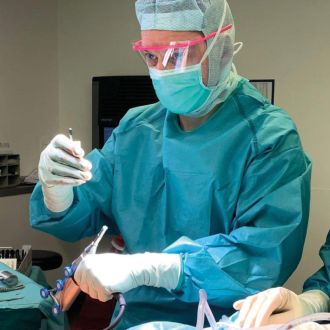 Chirurg in OP-Kleidung arbeitet mit einem robotergestützten Instrument am Knie eines Patienten im Operationssaal.