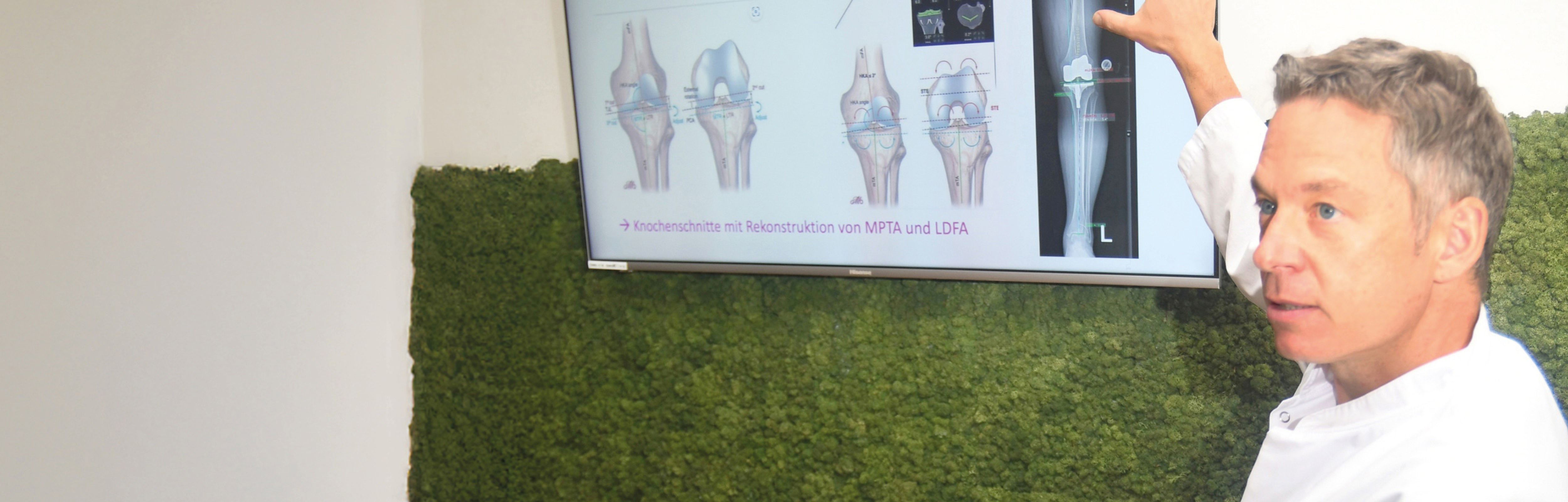 Dr. med. Andreas Bell zeigt auf eine Präsentation an einem Bildschirm.