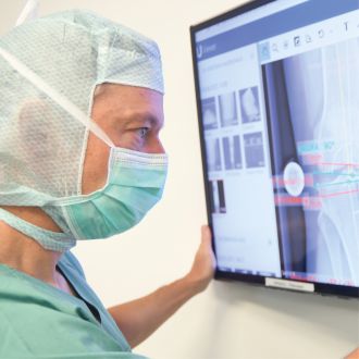 Dr. med. Andreas Bell in OP Kleidung schaut Röntgenbilder eines Kniegelenks auf Monitor an.