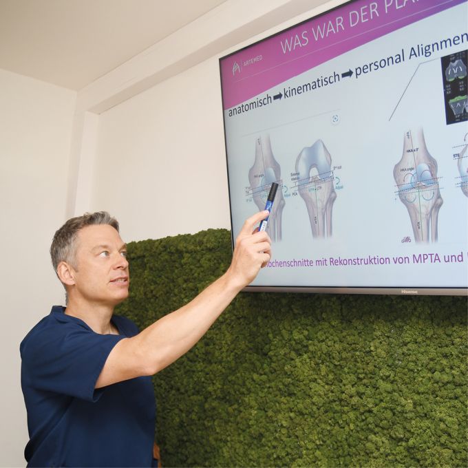 Dr. med. Andreas Bell zeigt auf eine Präsentation an einem Bildschirm.