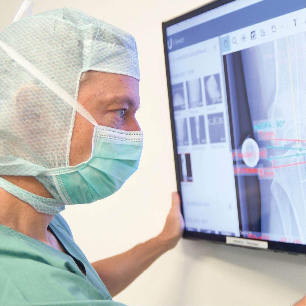 Dr. med. Andreas Bell in OP Kleidung schaut Röntgenbilder eines Kniegelenks auf Monitor an.