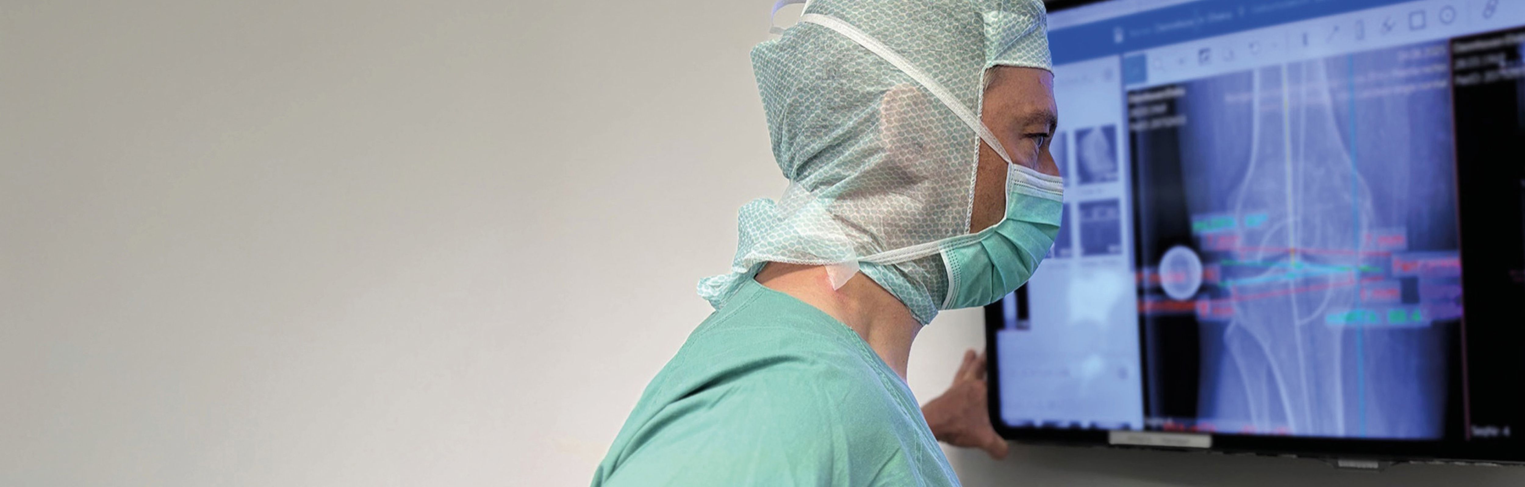 Arzt betrachtet Röntgenaufnahme eines Kniegelenks am Monitor.