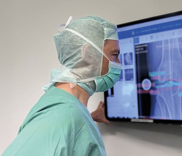 Dr. med. Andreas Bell in OP Kleidung schaut Röntgenbilder eines Kniegelenks auf Monitor an.