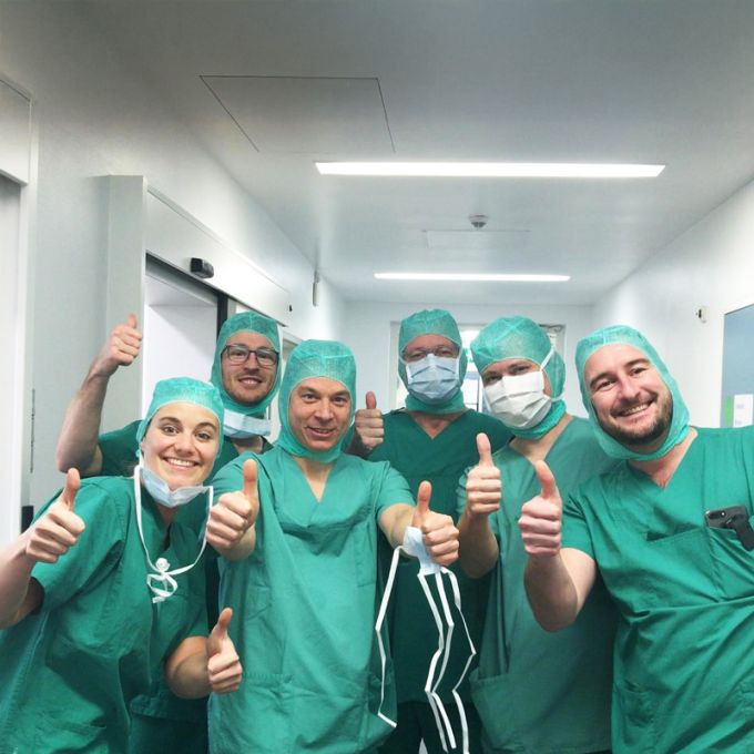 Gruppe von Klinikmitarbeitern in OP-Kleidung steht gemeinsam auf einem Flur.