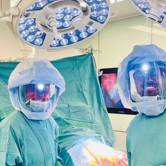 Zwei Chirurgen in OP-Kleidung stehen im Operationssaal unter OP-Lampen.