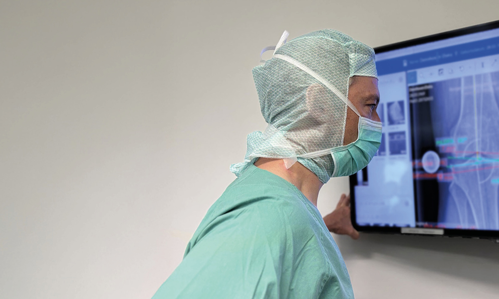 Dr. med. Andreas Bell in OP Kleidung schaut Röntgenbilder eines Kniegelenks auf Monitor an.