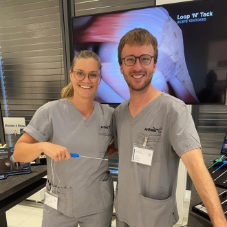 Zwei Personen in medizinischer Arbeitskleidung stehen vor einem Bildschirm mit anatomischer Darstellung.